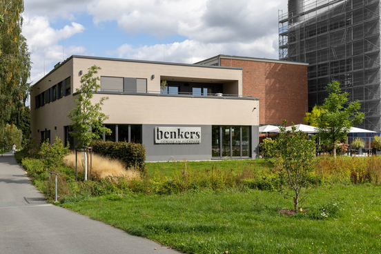 Modernes zweigeteiltes Gebäude als Restaurant und Wohneinheit in Marktredwitz mit Flachdach und großer Fensterfront, links Schriftzug 'benkers',Terrasse mit Sonnenschirmen und Bäumen