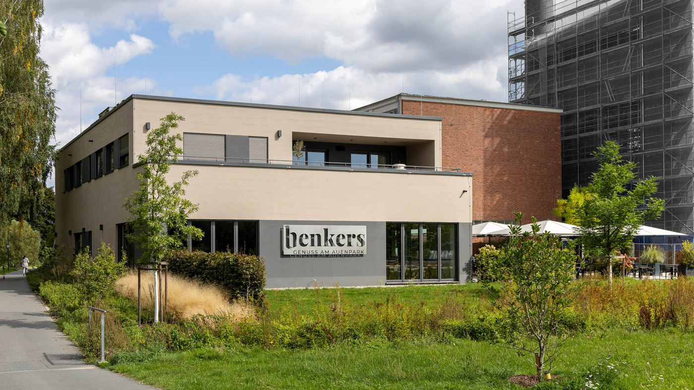 Modernes zweigeteiltes Gebäude als Restaurant und Wohneinheit in Marktredwitz  mit Flachdach und großer Fensterfront, links Schriftzug 'benkers',Terrasse mit Sonnenschirmen und Bäumen