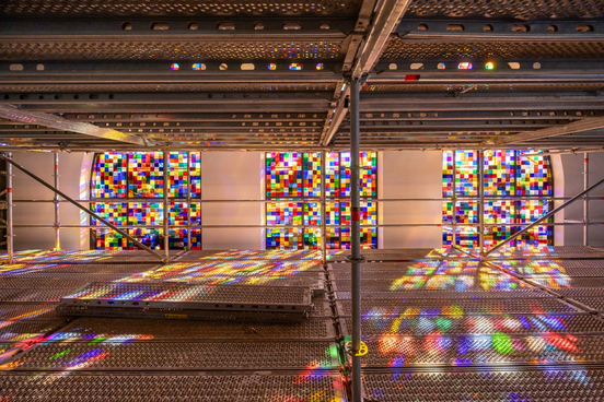 Blick durch ein Gerüst auf bunte Glasfenster und deren farbige Lichtreflexe auf dem Gerüstboden