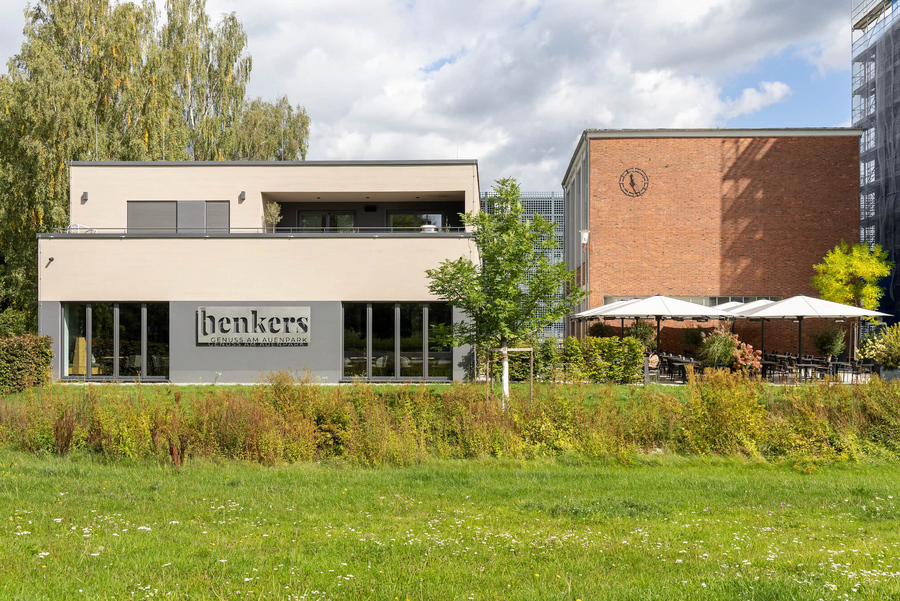Moderner Neubau mit Restaurant benkers und Wohneinheit mit weißer Fassade, davor Wiese und Bäume