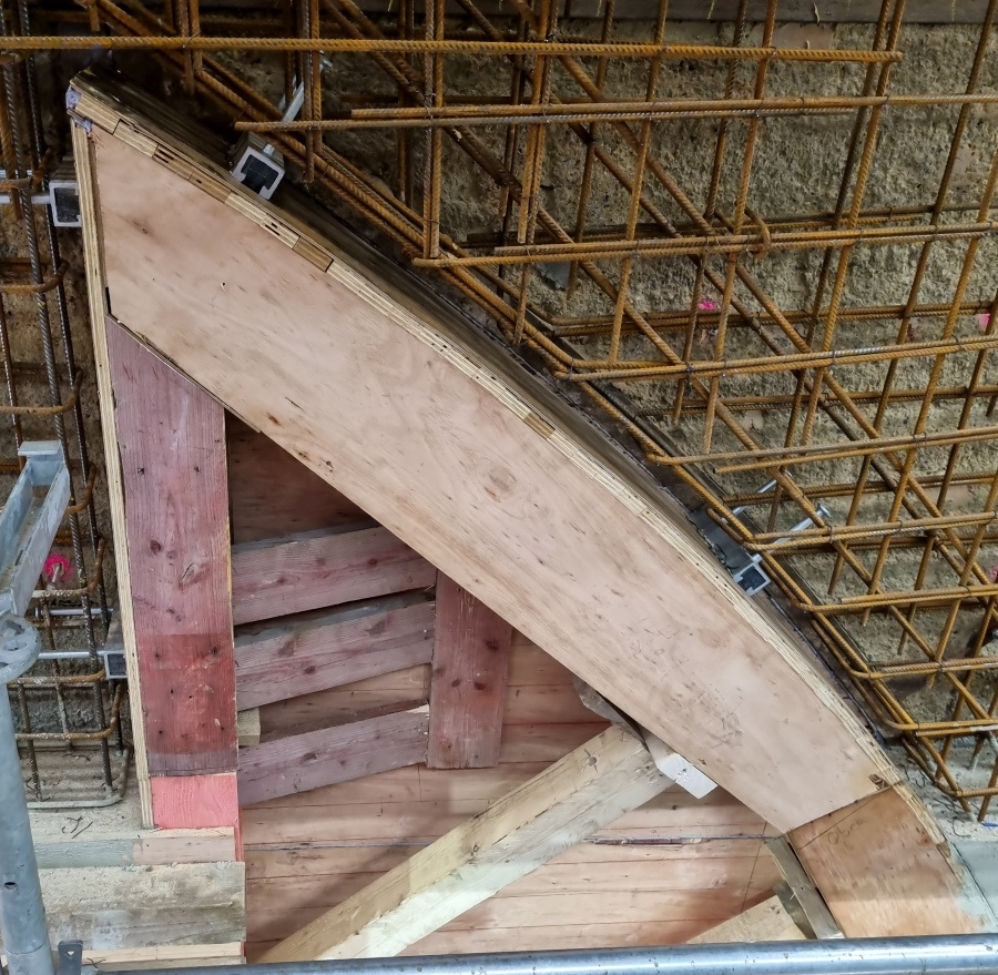 Detail einer gebogenem Holzschalung und Stahlarmierung im Hintergrund