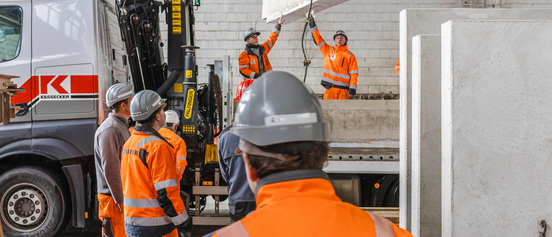 Fünf Auszubildende bei Kassecker verladen Betonteile auf einen LKW Anhänger.