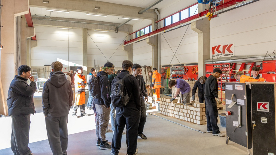 Gruppe von Jugendlichen beobachtet in der KASSECKER Ausbildungshalle zwei Personen beim Mauern einer Wand aus Ziegelsteinen